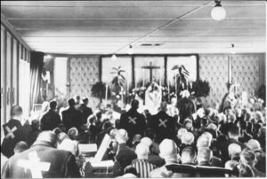 Historische Aufnahme einer Messe in einer Kapelle im Jahr 1944, vermutlich mit Häftlingen, die in einer gefüllten Kapelle dem Gottesdienst beiwohnen