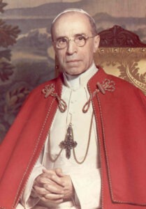 Papst Pius XII. in rotem Umhang mit goldenen Verzierungen, ernst blickend und die Hände gefaltet