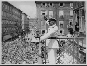 Benito Mussolini grüßt 1939 von einem Balkon eine große Menschenmenge in einer italienischen Stadt. Historisches Schwarz-Weiß-Foto aus der Zeit des faschistischen Italiens.