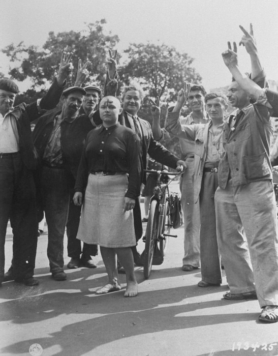 Members of the French resistance display the sign of victory beside a woman whose hair was shorn